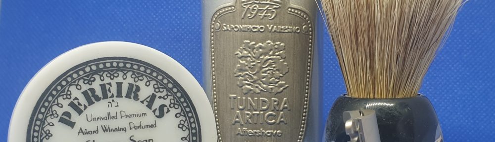 On a blue background: in front a Tatara razor. Behind it, from left to right, a small tub of Pereira soap, a aluminium bottle of aftershave, and a vie long brush